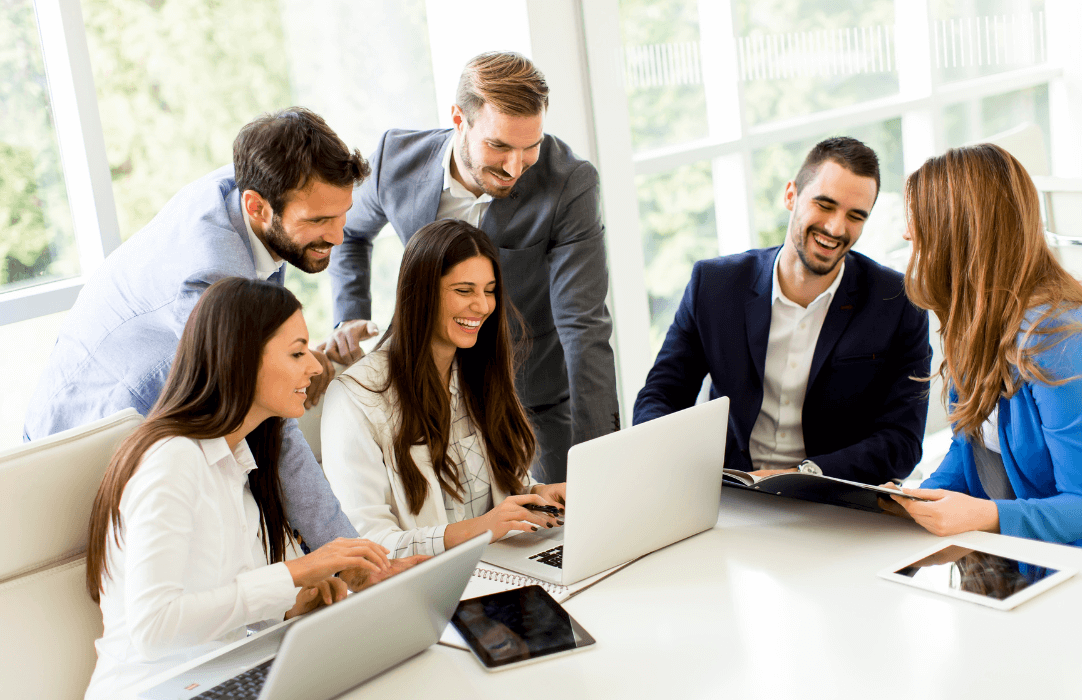Business team looking at a laptop and smiling around a boardroom table