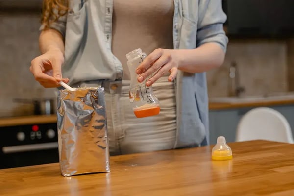A parent preparing a baby bottle with powdered formula in a kitchen