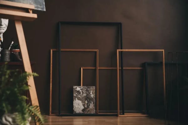 Empty picture frames leaning against a wall in a dimly lit studio