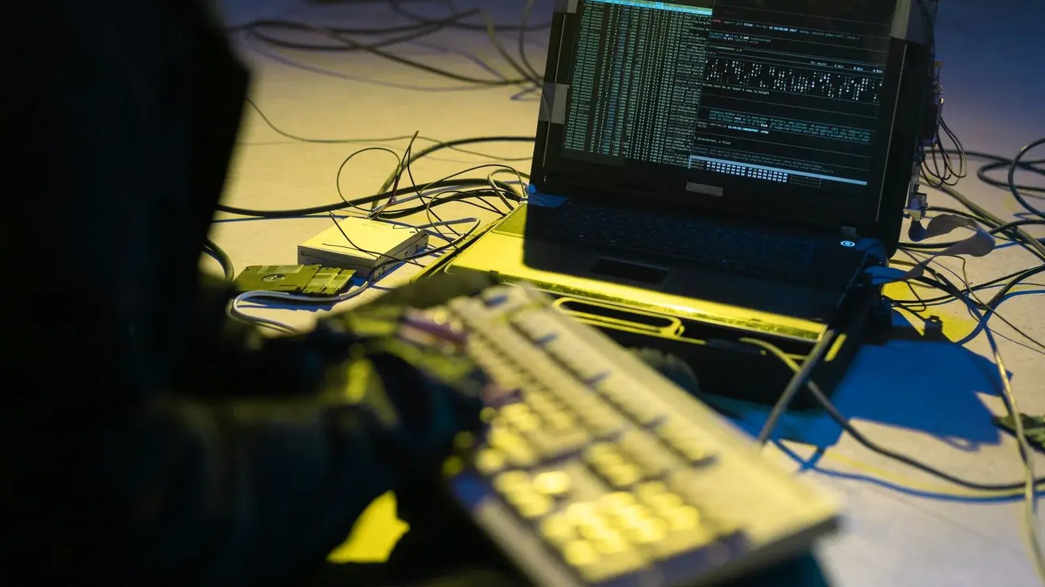 An unattended laptop and keyboard on a desk, surrounded by cables