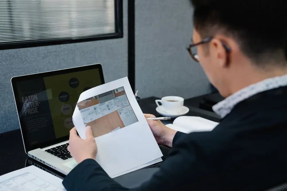 Professional reviewing a document beside a laptop