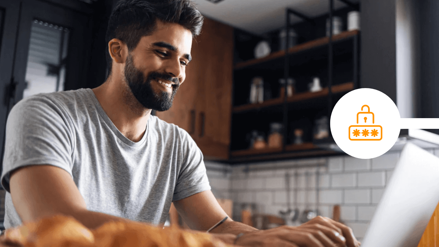 A man smiles while using a laptop in his kitchen, beside a padlock and password icon representing email attachment encryption