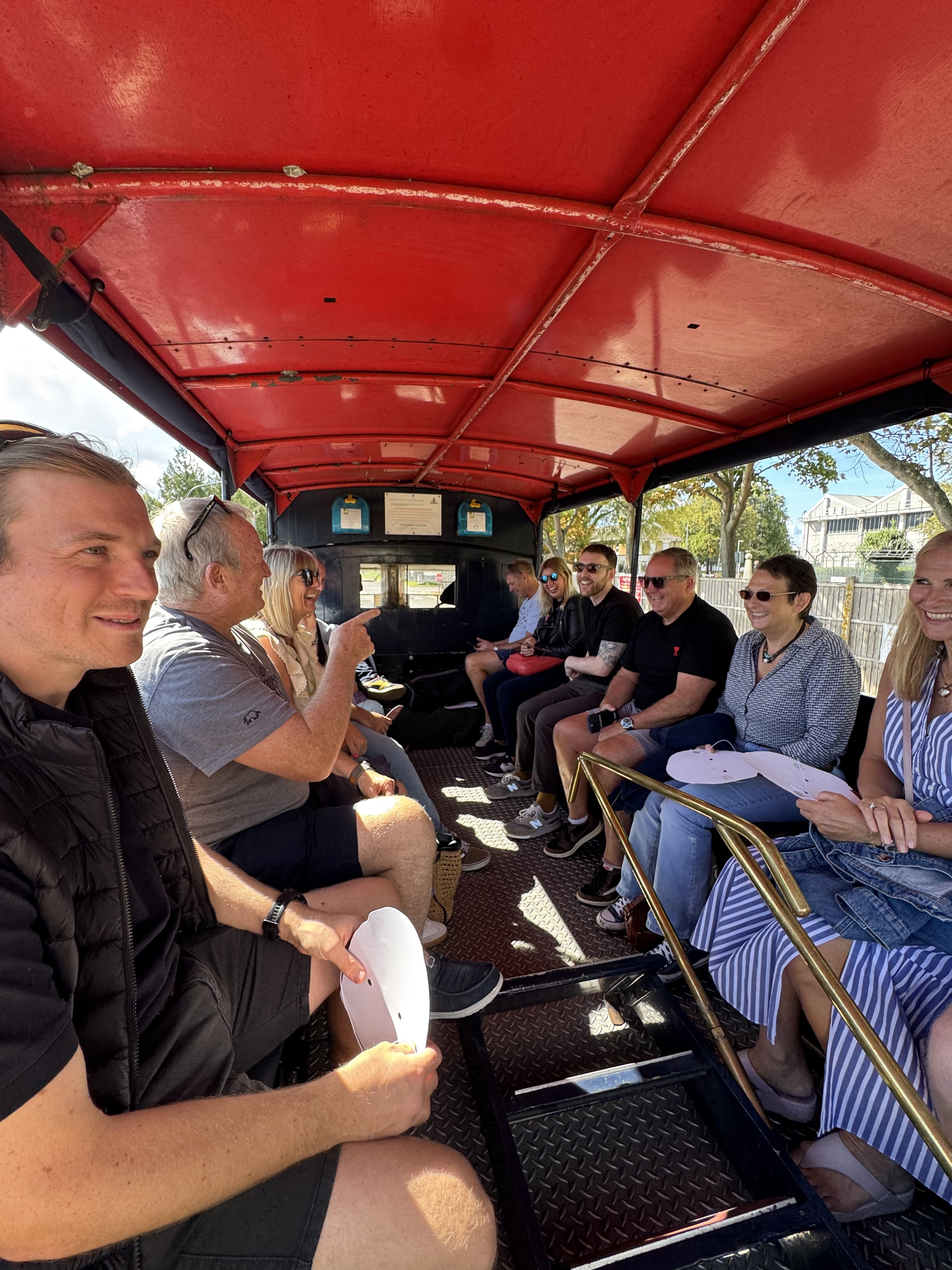The Beyond Encryption team sitting together on a vintage open-top vehicle in the sunshine, celebrating CEO Paul Holland's birthday
